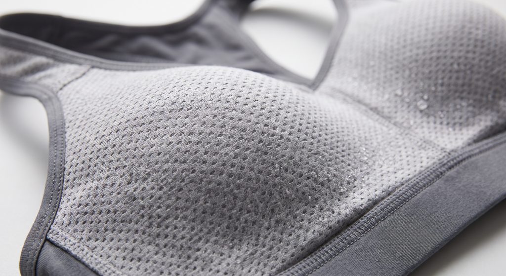 A macro photograph detailing light grey bird's eye mesh fabric used as a sports bra lining, highlighting the distinct pinhole pattern for ventilation and moisture wicking.