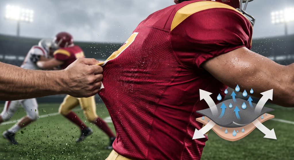 Close-up photograph of dynamic high-performance football jersey mesh fabric wicking sweat and stretching under contact in a stadium game.