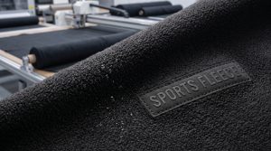 Close-up texture of high-performance black sports fleece fabric showing brushed pile and moisture-wicking water droplets for activewear.